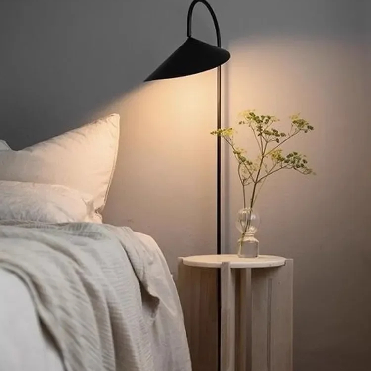 Grande lampe champignon murale en métal dans une chambre avec un lit blanc à gauche et une plante à droite