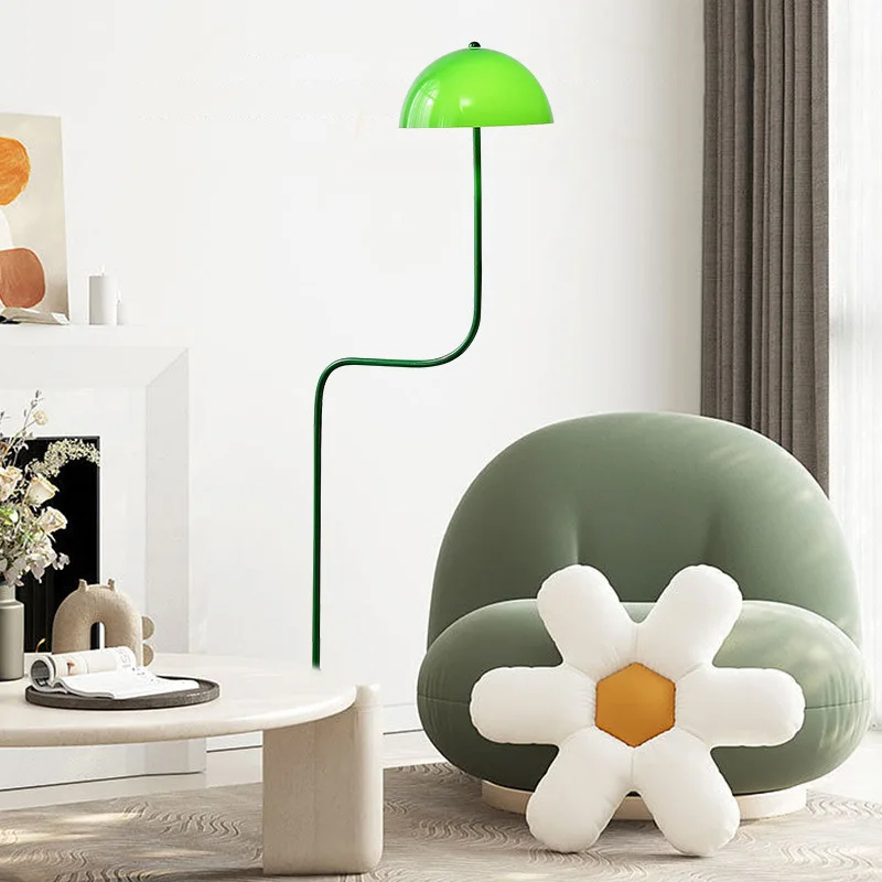 Lampadaire champignon vert de style original en métal sur fond blanc avec un fauteuil vert et une grosse pâquerette devant en coussin