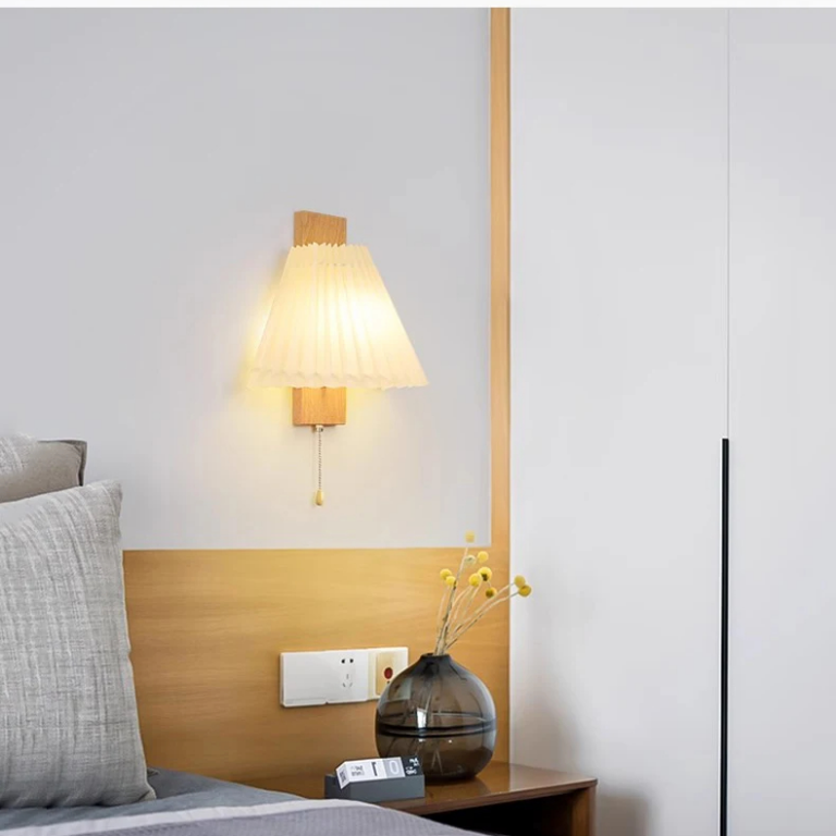 Lampe champignon murale en tissu plissé sur fond gris au dessus d'un lit et une table de nuit