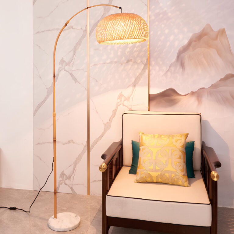 Lampadaire avec socle imitation marbre, tige peinte style bambou et abat-jour en forme de cloche en rotin. Au-dessus d'un fauteuil style chinois avec coussins blanc. Contre un mur avec motifs de montagnes rocheuses.