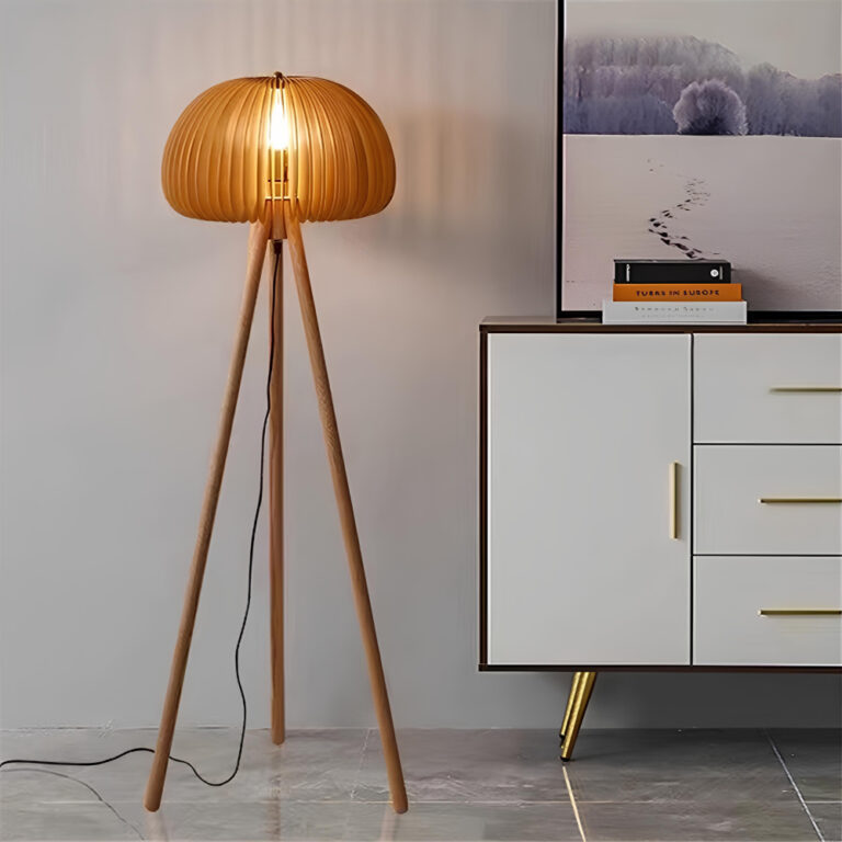 Lampadaire champignon en bois avec trépied large et sphère en bois ajourée laissant passer la lumière A droite un buffet blanc avec une porte a gauche et trois tiroirs Un mur blanc derrière le lampadaire Un cadre au-dessus du buffet.