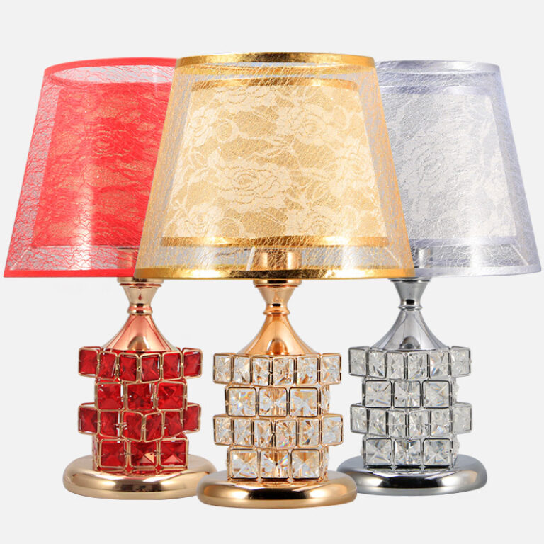 Trois lampe champignon avec socle rond, quatre rangées de carrés donnant un effet de diamants et au-dessus un double abat-jour. Celui du dessus est transparent, celui d'en-dessous a des motifs floraux. La lampe de gauche est rouge, celle du milieu est dorée et celle de droite est grise. Sur fond blanc.