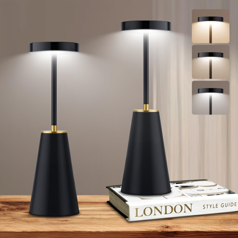 Deux lampes champignon de couleur noire avec le pied en forme de cône, une tige et un chapeau plat diffusant la lumière par le dessous. La lampe de droite est posé sur un livre blanc où est écrit "London". A droite, il y a 3 carrés montrant les différentes couleurs de lumière. Elles sont posées sur un support en bois, le mur est beige.