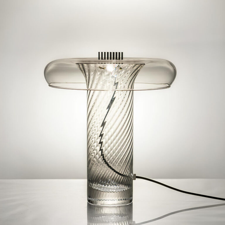 Lampe champignon en verre soufflé. Son corps en forme de cylindre est en verre torsadé transparent. Le fil passe à travers le tube avec à l'extrémité la source lumineuse. Le chapeau en verre se replit vers l'extérieur. L'ampoule est allumée.