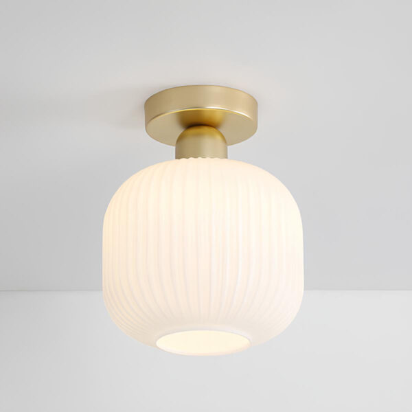 Plafonnier champignon avec socle doré et abat-jour carré arrondi en verre blanc. L'ampoule est allumée. Fixé sur un plafond blanc.